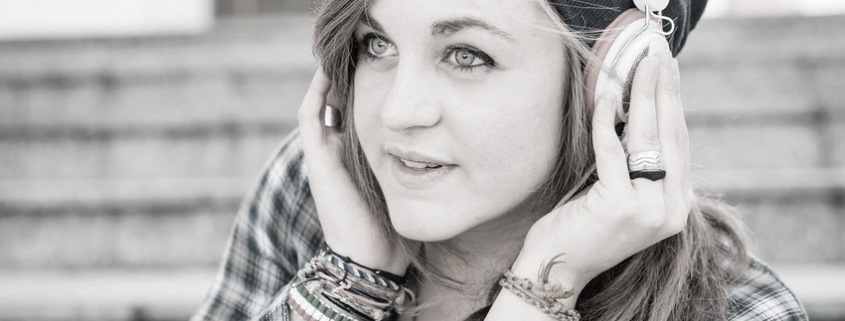 A woman wearing headphones and a plaid shirt outdoors.